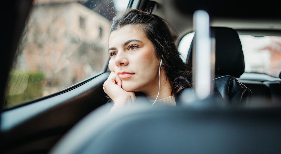 A passenger in the back of a car while someone is learning to drive, wondering whether the driver needs specific learner driver insurance.
